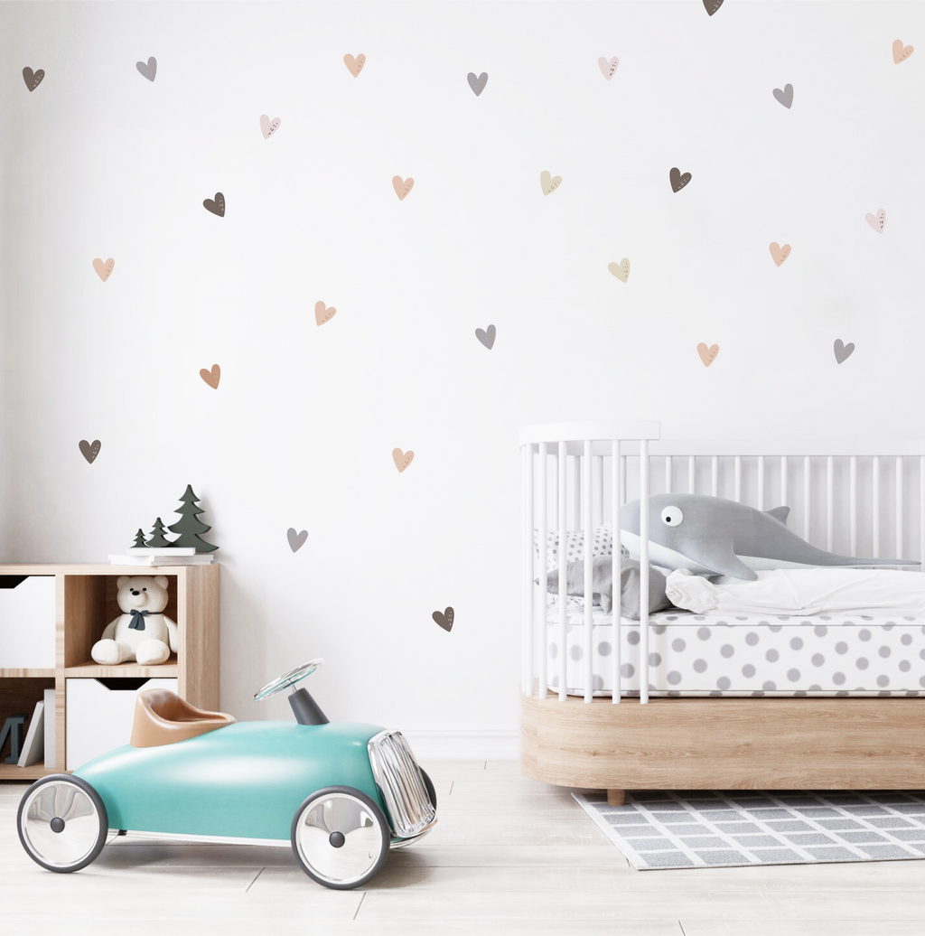 Soft neutral-tone heart decals scattered on a nursery wall above a wooden toy shelf and teddy bear